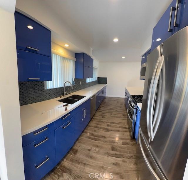 kitchen featuring sink, blue cabinetry, appliances with stainless steel finishes, dark hardwood / wood-style floors, and tasteful backsplash