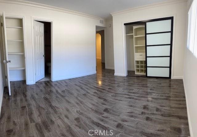 unfurnished bedroom with multiple closets, ornamental molding, and dark hardwood / wood-style floors