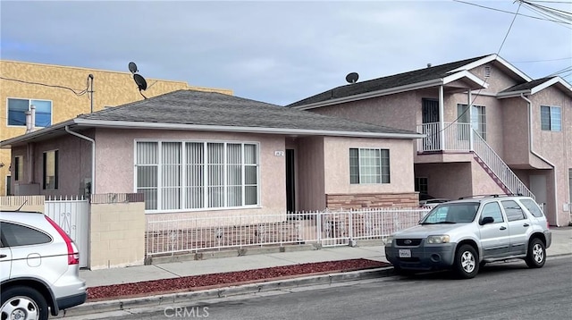 townhome / multi-family property with roof with shingles, fence, and stucco siding