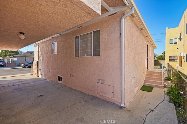 view of side of property featuring crawl space, fence, and stucco siding