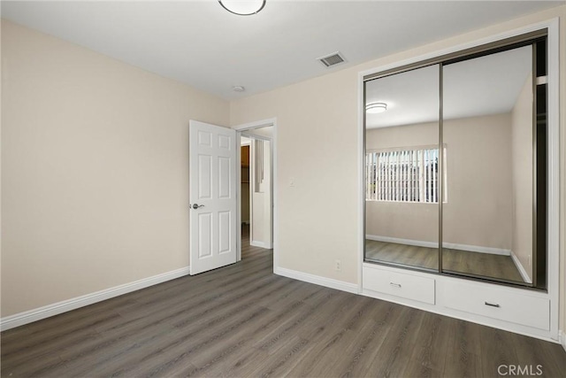 unfurnished bedroom with a closet, visible vents, dark wood finished floors, and baseboards