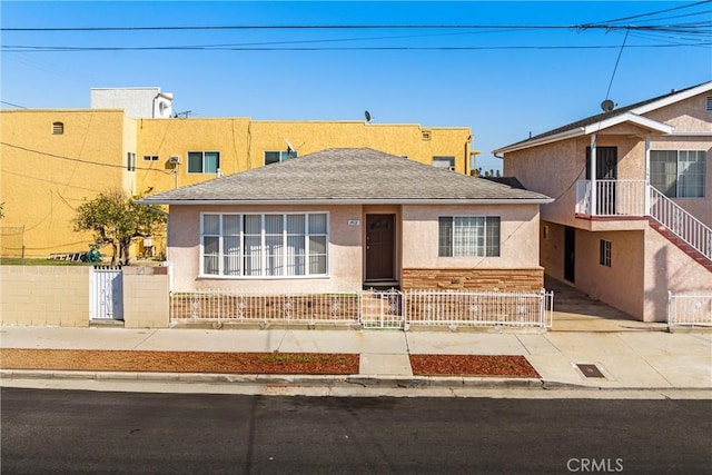 view of front of home featuring roof with shingles, a fenced front yard, and stucco siding