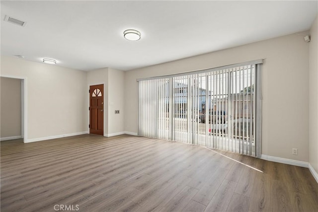 empty room featuring dark wood-style flooring, visible vents, and baseboards