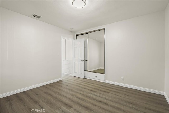 unfurnished bedroom with baseboards, visible vents, dark wood finished floors, and a closet