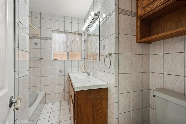 bathroom featuring a tub to relax in, toilet, vanity, tile walls, and tile patterned floors