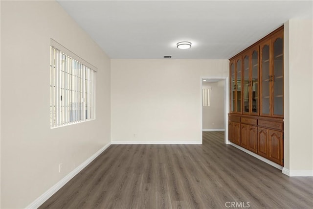 unfurnished room featuring dark wood-style floors, visible vents, and baseboards