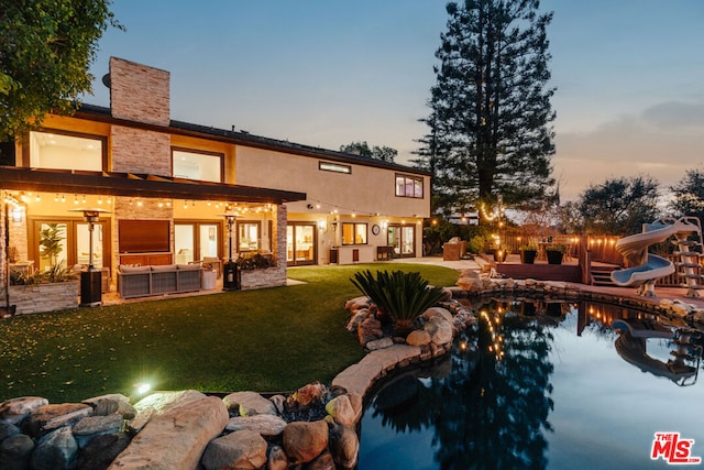 back house at dusk featuring a patio, outdoor lounge area, and a lawn