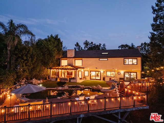 back house at dusk with a wooden deck and an outdoor living space