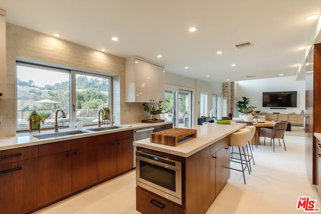 kitchen with a breakfast bar area, appliances with stainless steel finishes, white cabinetry, backsplash, and a kitchen island