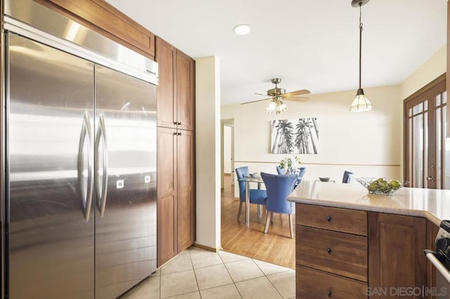 kitchen featuring built in refrigerator, hanging light fixtures, light tile patterned floors, ceiling fan, and stove