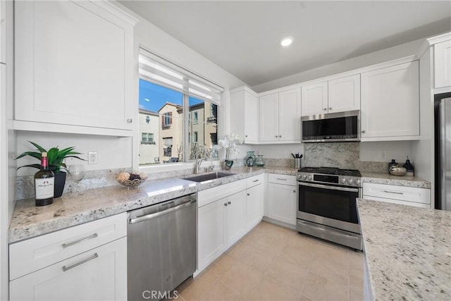 kitchen featuring sink, light tile patterned floors, appliances with stainless steel finishes, white cabinetry, and light stone countertops