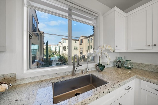 kitchen with light stone countertops, sink, and white cabinets