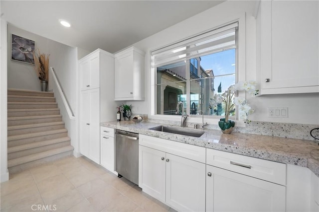 kitchen with white cabinetry, sink, stainless steel dishwasher, light tile patterned floors, and light stone countertops