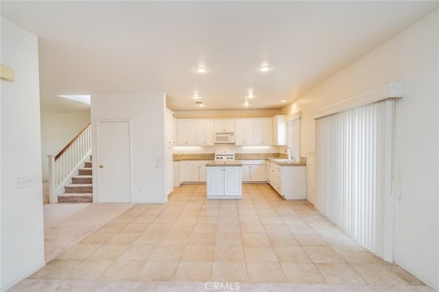 kitchen with light tile patterned flooring, sink, white cabinetry, a center island, and stove