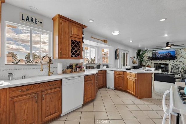 kitchen featuring a stone fireplace, tasteful backsplash, light tile patterned floors, white dishwasher, and kitchen peninsula