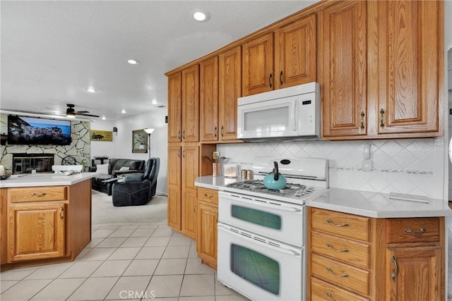 kitchen featuring a fireplace, decorative backsplash, light tile patterned floors, ceiling fan, and white appliances