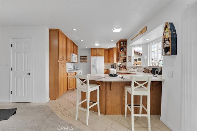 kitchen with white appliances, a breakfast bar, kitchen peninsula, and light tile patterned floors