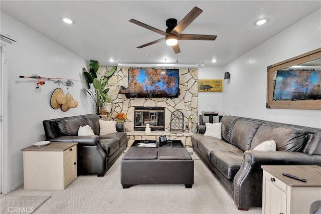 carpeted living room with a stone fireplace and ceiling fan