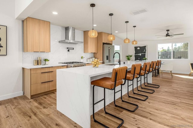 kitchen featuring appliances with stainless steel finishes, hanging light fixtures, backsplash, a center island with sink, and wall chimney exhaust hood