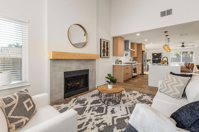 living room featuring a fireplace, a towering ceiling, light hardwood / wood-style flooring, and ceiling fan