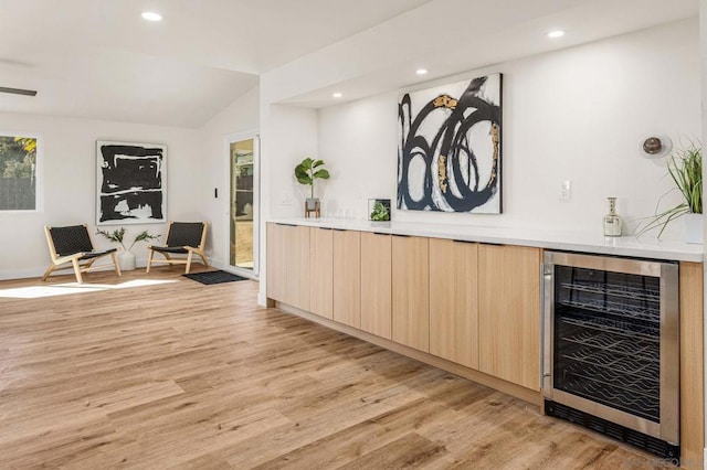 bar with lofted ceiling, light wood-type flooring, beverage cooler, and light brown cabinetry