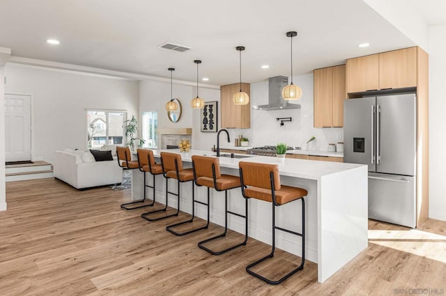 kitchen with appliances with stainless steel finishes, sink, hanging light fixtures, a center island with sink, and wall chimney range hood