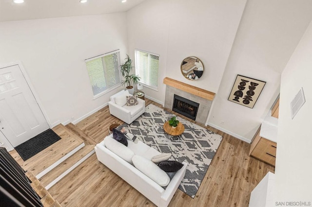 living room with a tiled fireplace, a towering ceiling, and light hardwood / wood-style flooring