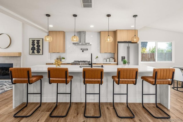 kitchen with pendant lighting, wall chimney range hood, high end refrigerator, and light brown cabinets