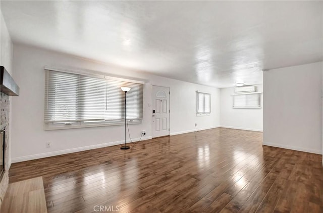 unfurnished living room with dark wood-type flooring, a stone fireplace, and a wall mounted AC