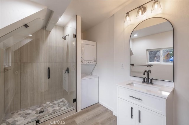 bathroom with a shower with door, stacked washing maching and dryer, hardwood / wood-style flooring, and vanity