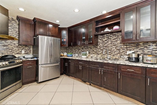 1230 Sunshine Dr, Barstow, CA 92311 - kitchen with wall chimney range hood, light tile patterned floors, stainless steel appliances, dark brown cabinetry, and light stone countertops