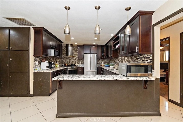 1230 Sunshine Dr, Barstow, CA 92311 - kitchen with light tile patterned floors, appliances with stainless steel finishes, hanging light fixtures, dark brown cabinets, and wall chimney exhaust hood