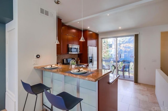 kitchen with a breakfast bar, tasteful backsplash, hanging light fixtures, kitchen peninsula, and stainless steel appliances