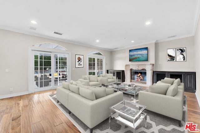 living room featuring a premium fireplace, crown molding, a healthy amount of sunlight, and light hardwood / wood-style flooring