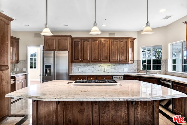 kitchen featuring sink, a center island, appliances with stainless steel finishes, pendant lighting, and light stone countertops