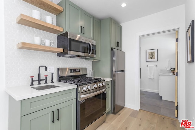 kitchen with tasteful backsplash, washer / dryer, sink, green cabinetry, and stainless steel appliances