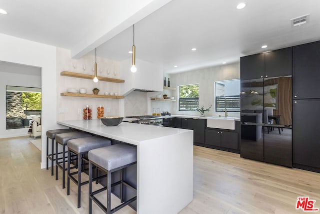 kitchen featuring a kitchen breakfast bar, kitchen peninsula, pendant lighting, light hardwood / wood-style floors, and stove