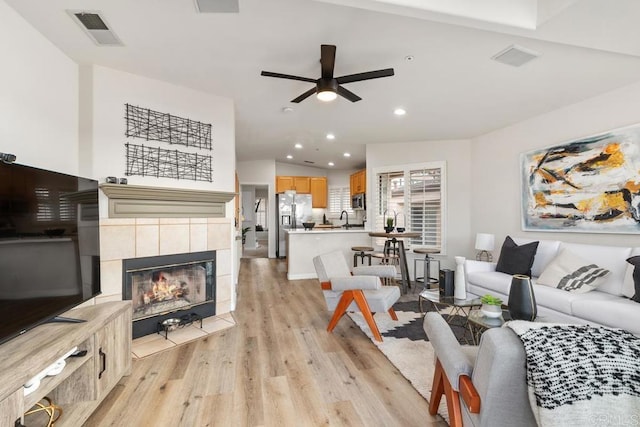 living room with a tiled fireplace, sink, light hardwood / wood-style flooring, and ceiling fan