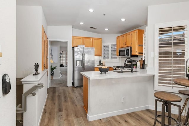 kitchen with sink, vaulted ceiling, light wood-type flooring, appliances with stainless steel finishes, and kitchen peninsula