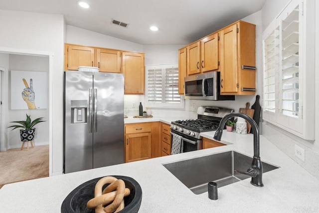 kitchen featuring appliances with stainless steel finishes, light brown cabinetry, sink, and carpet