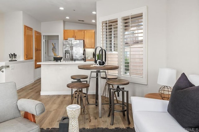 kitchen with vaulted ceiling, a kitchen bar, stainless steel fridge with ice dispenser, light brown cabinets, and light hardwood / wood-style flooring