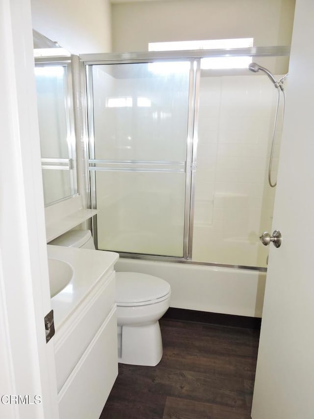 full bathroom featuring hardwood / wood-style flooring, vanity, shower / bath combination with glass door, and toilet