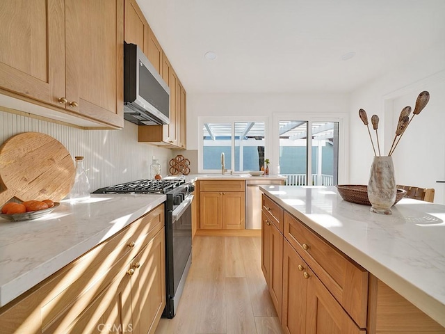 kitchen with sink, appliances with stainless steel finishes, light stone counters, light brown cabinets, and light wood-type flooring