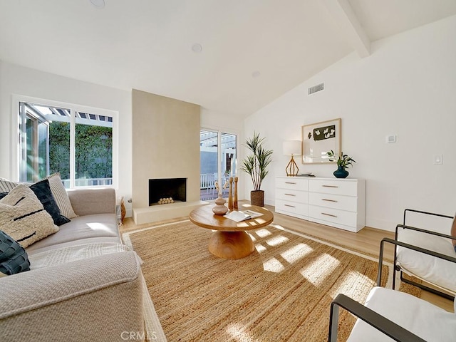 living room with lofted ceiling with beams, a fireplace, and light hardwood / wood-style floors