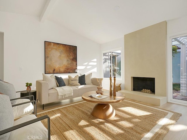 living room with vaulted ceiling with beams, a large fireplace, and light hardwood / wood-style flooring