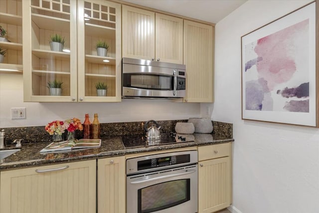 kitchen with light brown cabinetry, dark stone counters, and appliances with stainless steel finishes