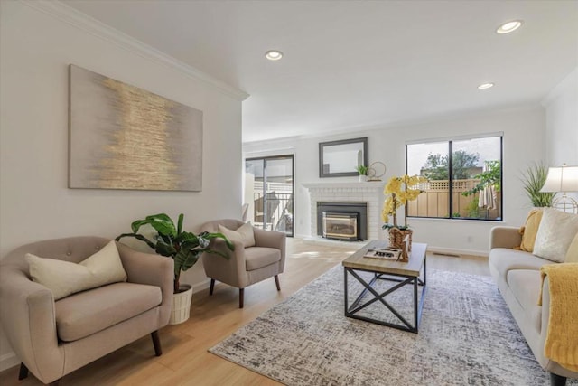 living room featuring ornamental molding, a brick fireplace, and light hardwood / wood-style floors