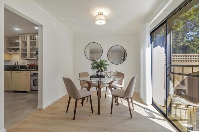 dining area with ornamental molding, sink, and light wood-type flooring