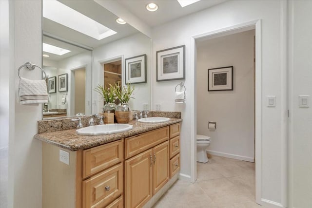 bathroom with vanity, toilet, a skylight, and tile patterned flooring