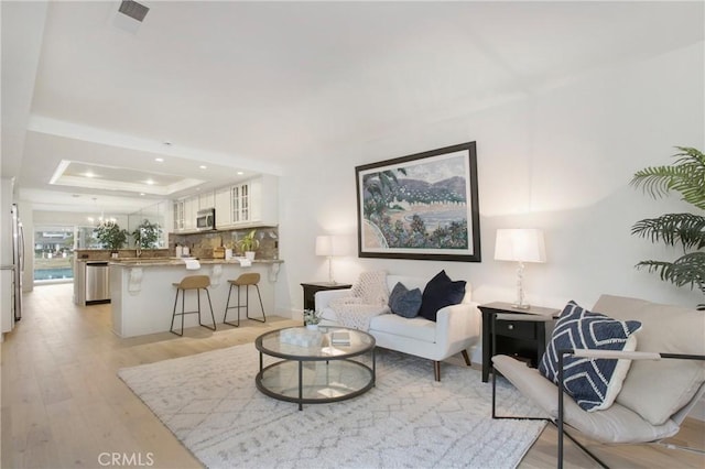 living room featuring an inviting chandelier, a tray ceiling, and light hardwood / wood-style floors